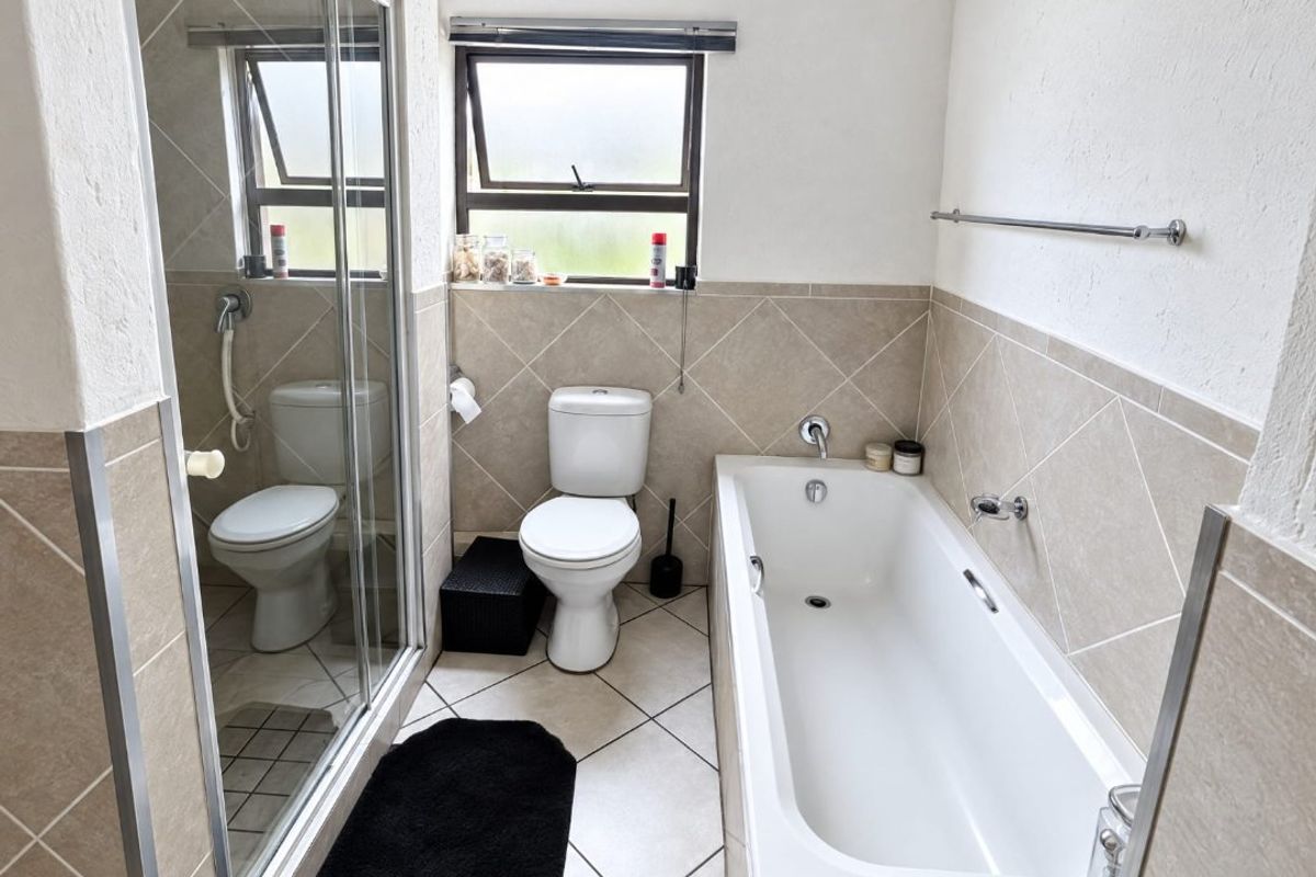 A functional bathroom featuring a bathtub, separate shower enclosure, toilet, and neutral tiled finishes throughout.