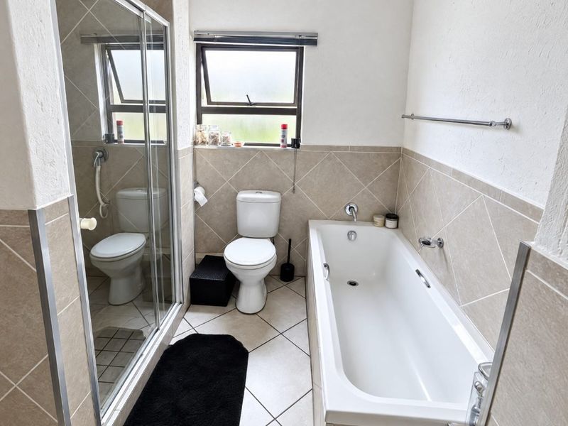 A functional bathroom featuring a bathtub, separate shower enclosure, toilet, and neutral tiled finishes throughout.