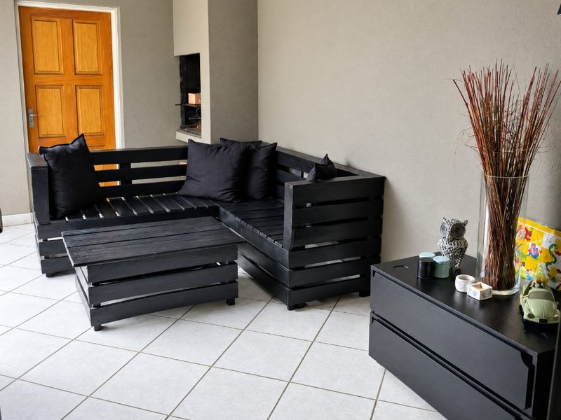 A covered patio area featuring tiled flooring, a built-in braai, and a wooden door leading to the interior.