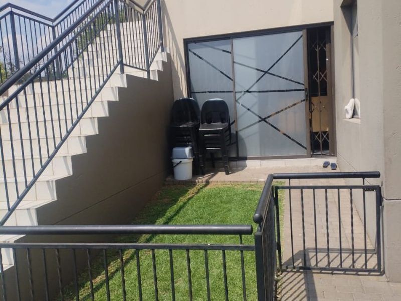Rear exterior view of the apartment featuring a small private lawn, paved patio area, and an external metal staircase leading to the upper level.