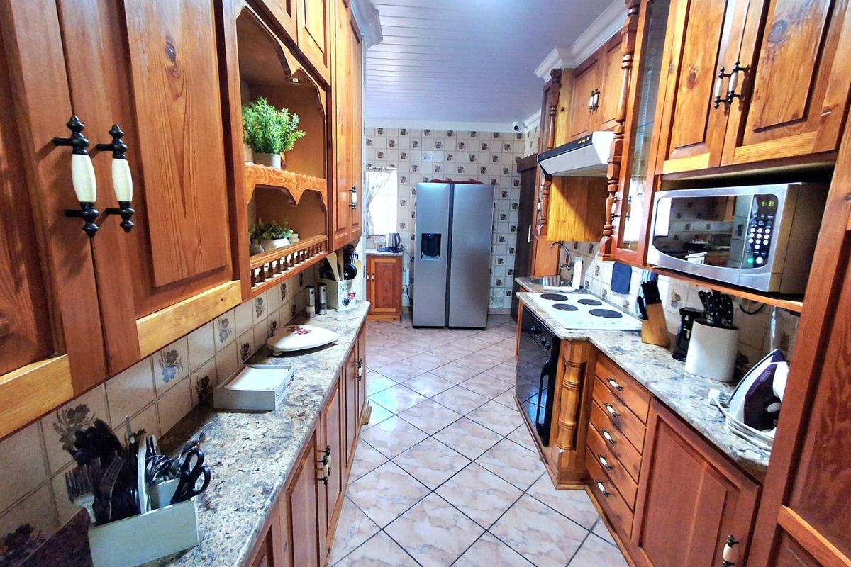 A functional galley-style kitchen featuring extensive wooden cabinetry, granite countertops, built-in appliances, and tiled flooring throughout.