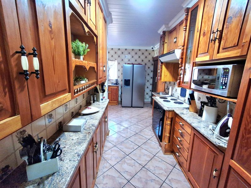 A functional galley-style kitchen featuring extensive wooden cabinetry, granite countertops, built-in appliances, and tiled flooring throughout.