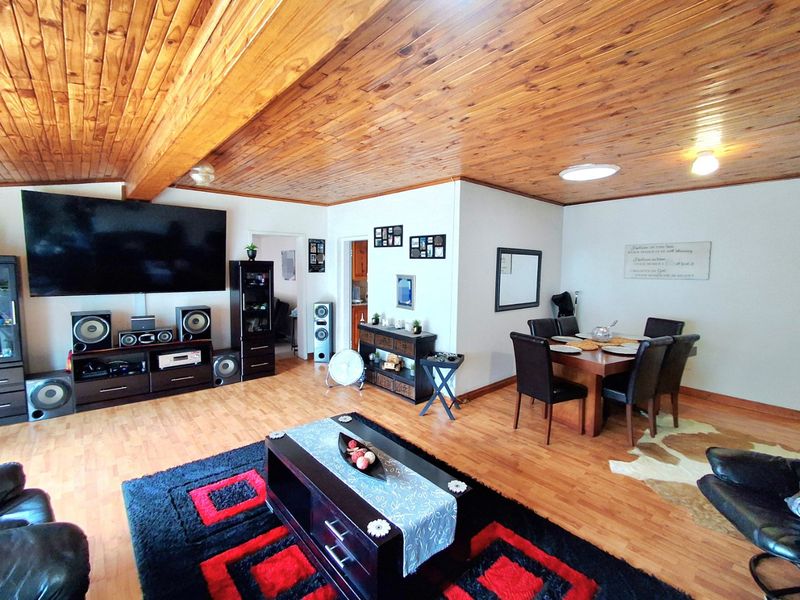 Spacious open-plan living and dining area featuring warm timber tongue and groove ceilings, exposed beams, and durable laminate flooring throughout.
