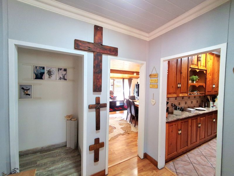 A central hallway providing access to a kitchen with timber cabinetry and a living area, featuring laminate flooring and coved ceiling details.
