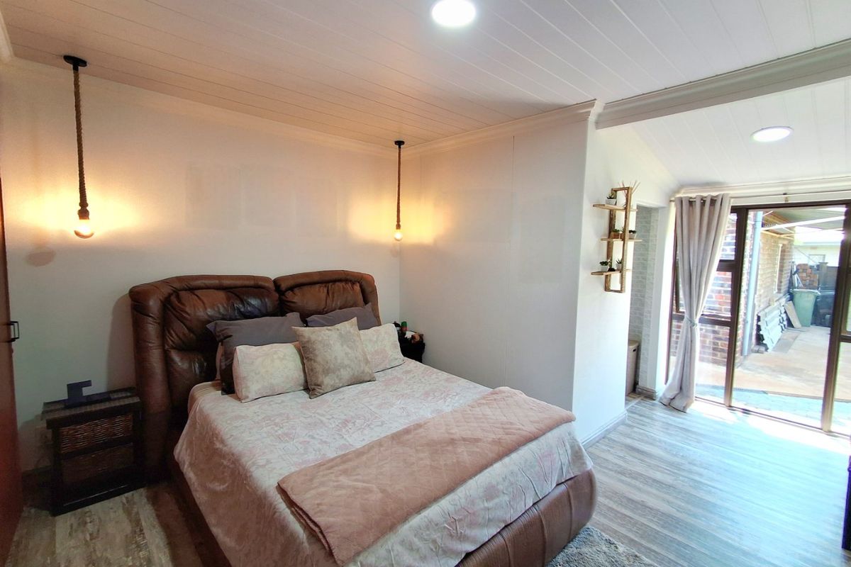 A well-maintained bedroom featuring modern timber-look flooring, tongue and groove ceiling, and direct access to an outdoor area through sliding glass doors.