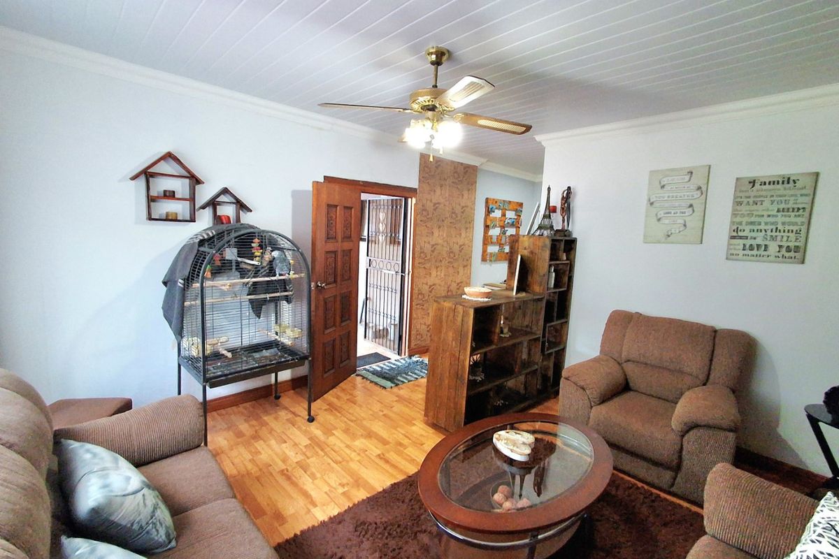 A living room featuring timber-look flooring, a ceiling fan, and a tongue and groove ceiling, with access to an exterior security gate.
