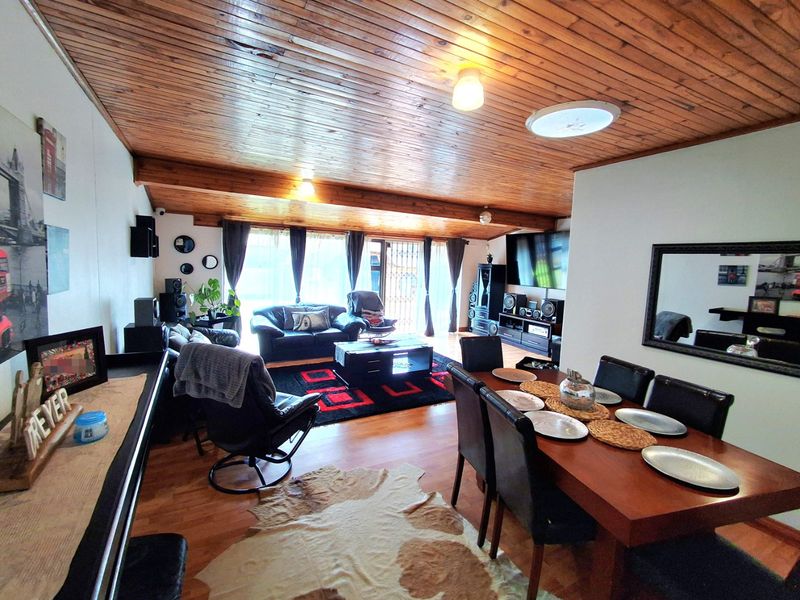Spacious open-plan living and dining area featuring a distinctive timber-clad vaulted ceiling, exposed beams, and direct access to the outdoors via sliding glass doors.