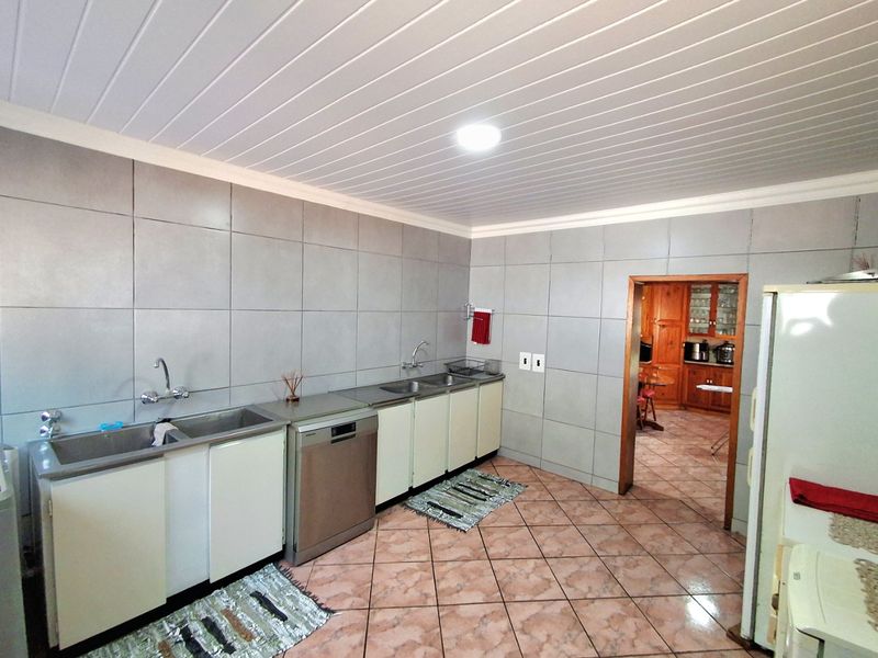 A functional kitchen featuring a double stainless steel sink, integrated dishwasher, tiled splashbacks, and tiled flooring, with a view into an adjacent room.