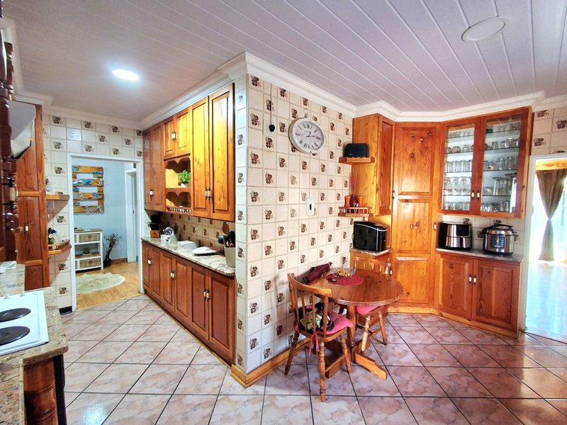 A spacious kitchen featuring extensive wooden cabinetry, granite countertops, decorative tiled backsplash, and tiled flooring with a classic, traditional aesthetic.