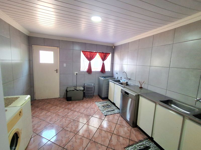 A functional laundry room featuring tiled walls and flooring, built-in cabinetry, and a stainless steel sink with plumbing connections for appliances.