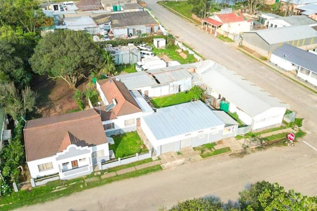 Aerial view of a residential property featuring a main house with a tiled roof, adjacent outbuildings, and a large yard area.