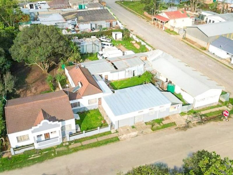 Aerial view of a residential property featuring a main house with a tiled roof, adjacent outbuildings, and a large yard area.
