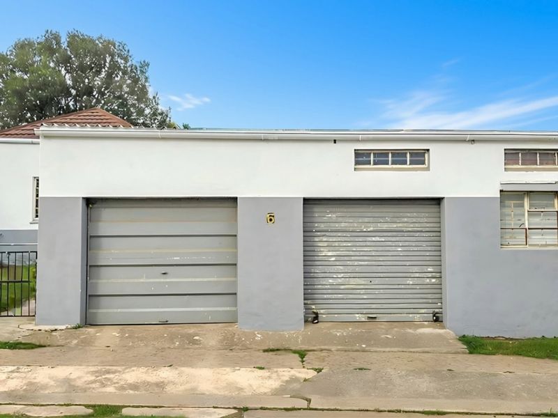 A double garage exterior featuring two roller doors, steel-framed windows, and a concrete driveway, showing signs of exterior wear and weathering.