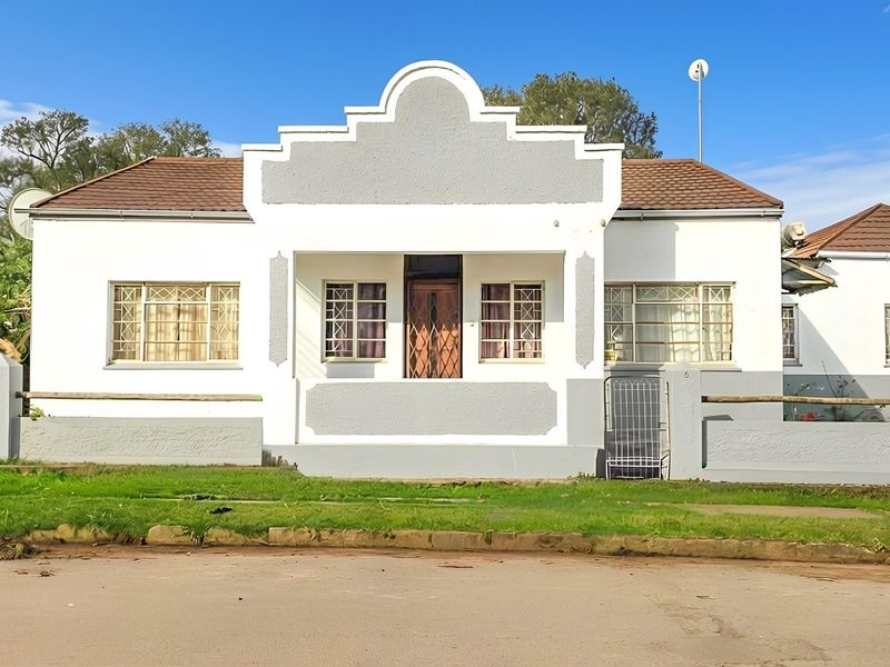 Front elevation of a single-story house featuring a covered porch, security bars on windows, and a perimeter boundary wall.