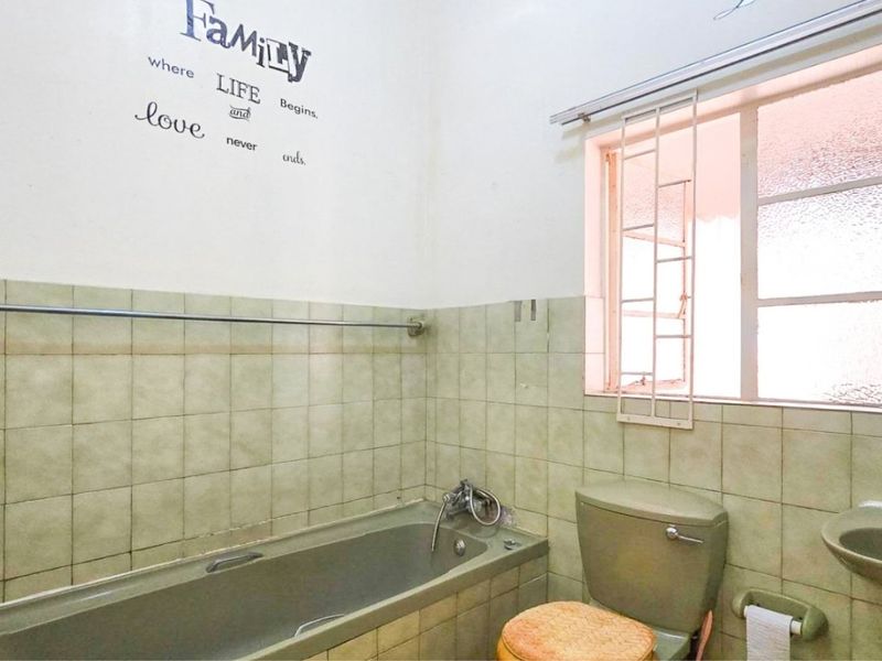 A dated bathroom featuring a bathtub, toilet, and wall-mounted basin with tiled walls and security bars on the window.
