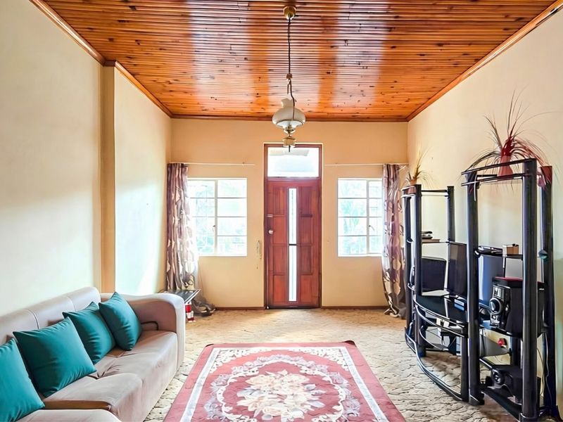 A living room featuring a timber tongue and groove ceiling, timber entrance door, and dual casement windows with carpet flooring.