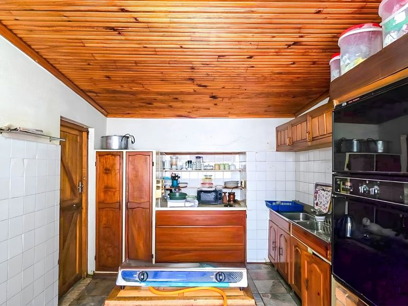 A dated kitchen featuring timber tongue and groove ceilings, built-in wooden cabinetry, tiled splashbacks, and an integrated eye-level oven.