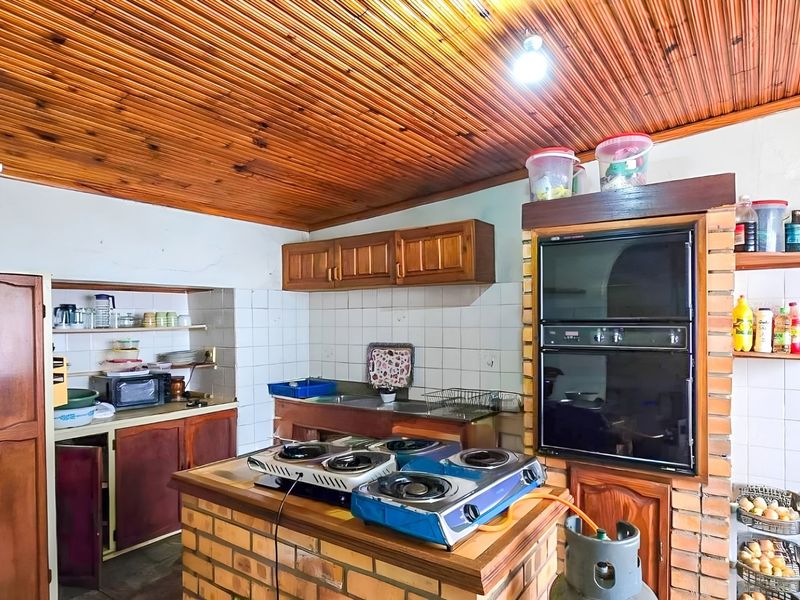 A rustic kitchen featuring a timber-clad ceiling, brick-built island and oven housing, and traditional wooden cabinetry with tiled splashbacks.