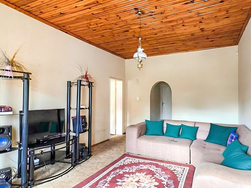 A living room featuring a distinctive timber tongue and groove ceiling, carpeted flooring, and an arched doorway leading to adjacent areas.