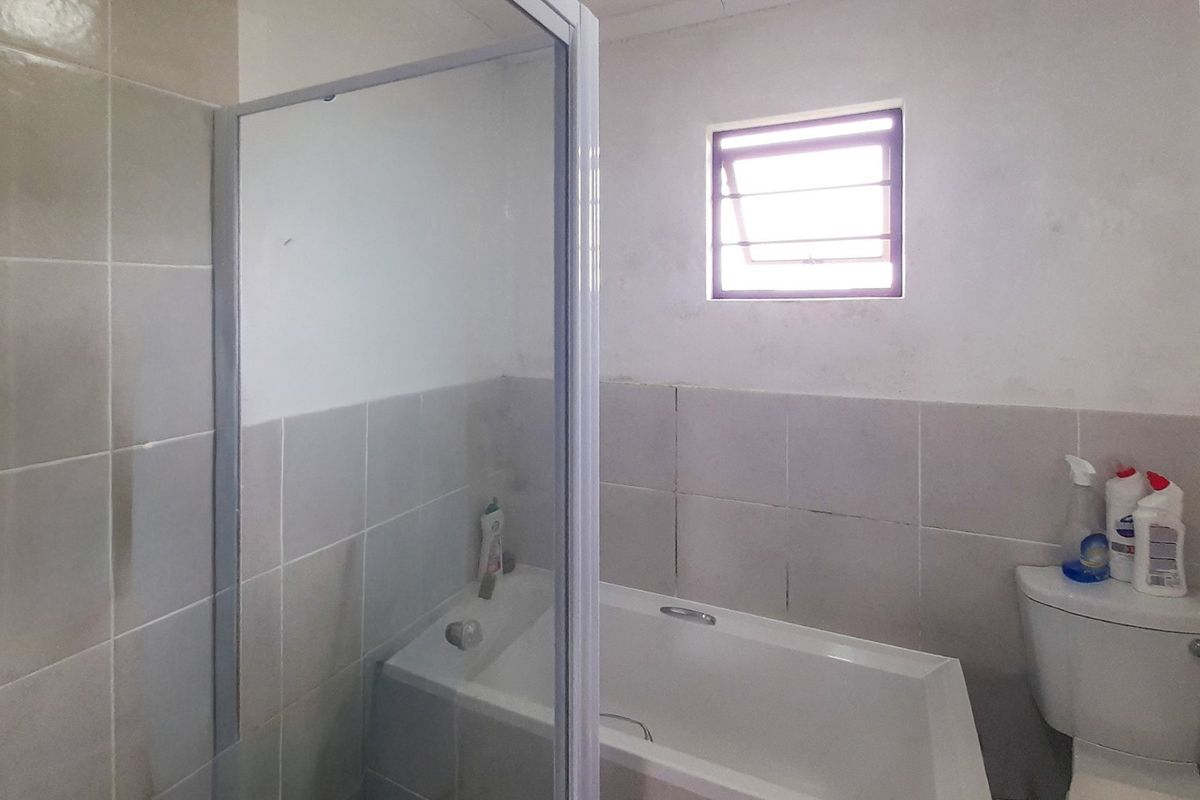 A functional bathroom featuring a bathtub, separate shower enclosure, and toilet, with neutral wall tiling and a louver window for ventilation.
