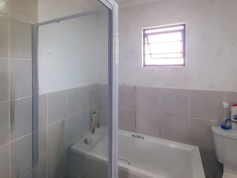 A functional bathroom featuring a bathtub, separate shower enclosure, and toilet, with neutral wall tiling and a louver window for ventilation.