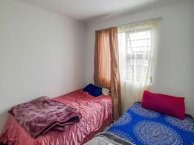 A compact bedroom featuring a built-in wardrobe and a window fitted with security bars.