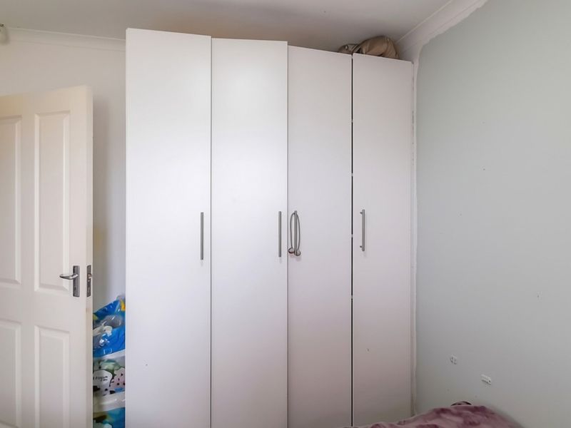 A bedroom featuring a white built-in wardrobe with modern handles and neutral wall finishes.
