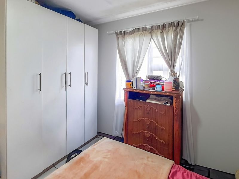 A bedroom featuring a large white built-in wardrobe and a window with a curtain rod.