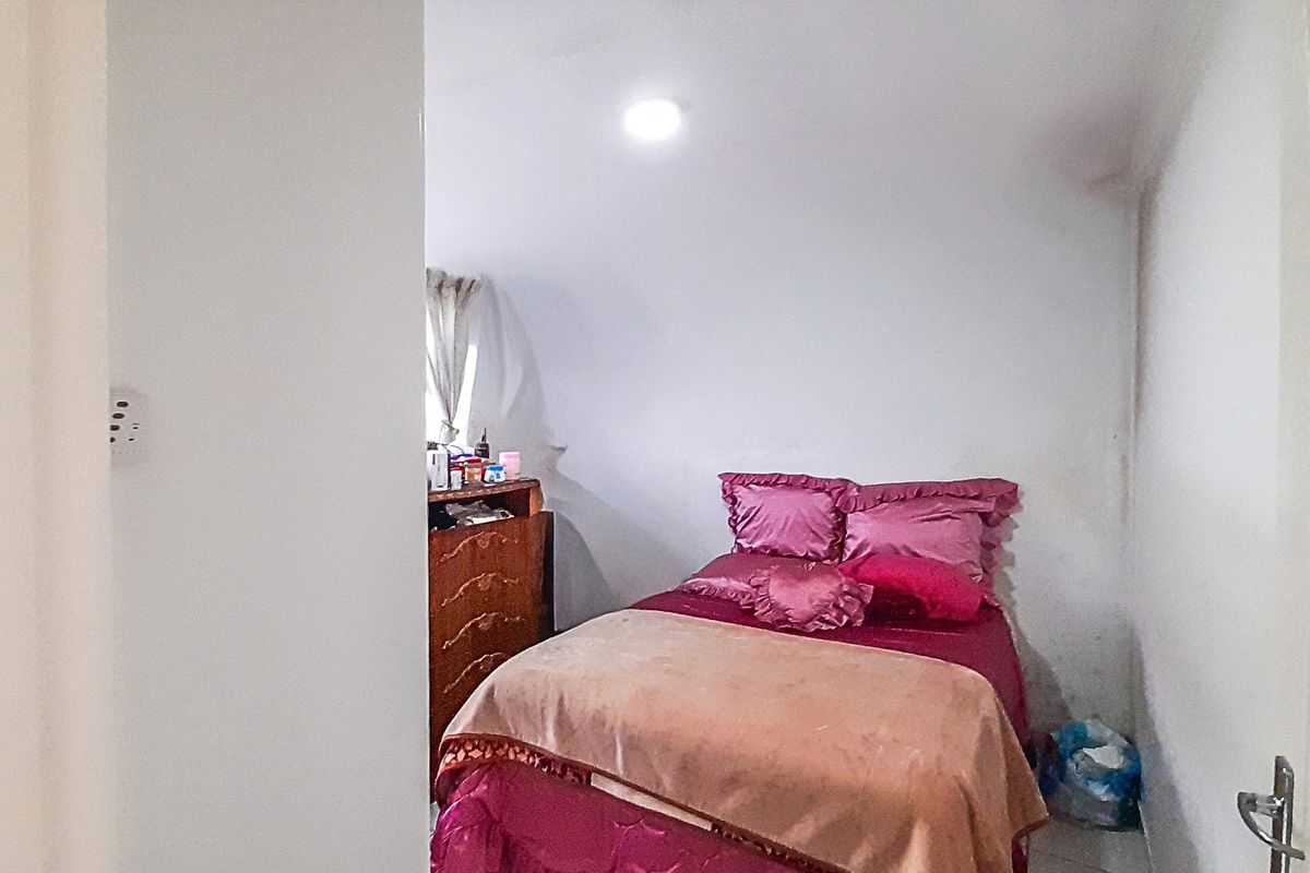 A compact bedroom featuring a window and recessed ceiling lighting, currently showing signs of wall wear and staining.