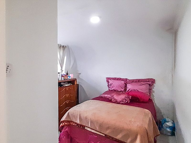 A compact bedroom featuring a window and recessed ceiling lighting, currently showing signs of wall wear and staining.
