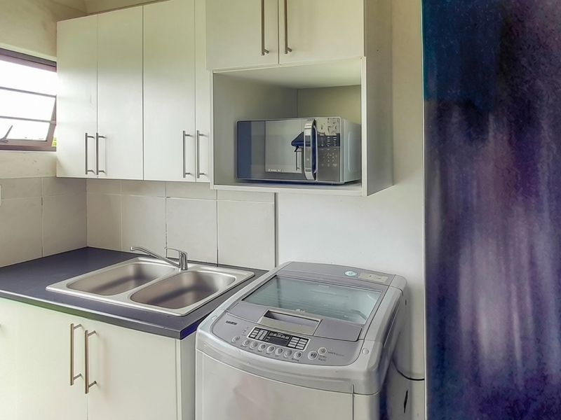 Functional laundry area featuring white built-in cabinetry, a double stainless steel sink, laminate countertops, and a tiled backsplash.