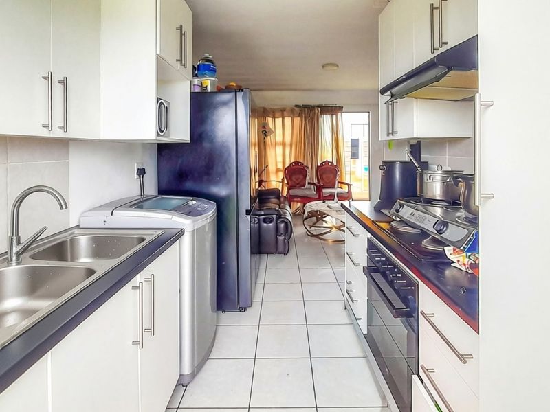 Open plan kitchen featuring white cabinetry, dark countertops, built-in oven, gas hob, and tiled flooring, flowing into the adjacent living area.