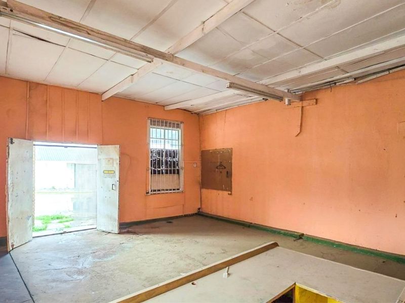 A vacant utility or commercial workspace featuring security-barred windows, a suspended ceiling, and a built-in counter, requiring significant cosmetic refurbishment.