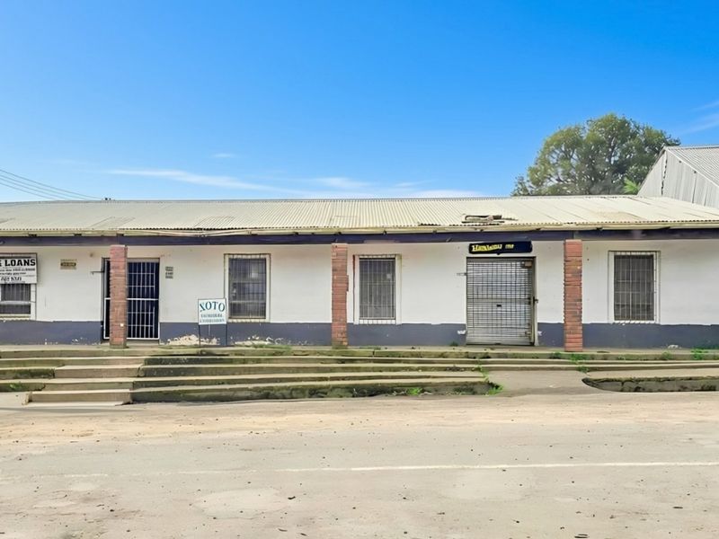 Commercial street-front property featuring a corrugated metal roof, brick pillars, and secure access points with roller shutters and security gates.