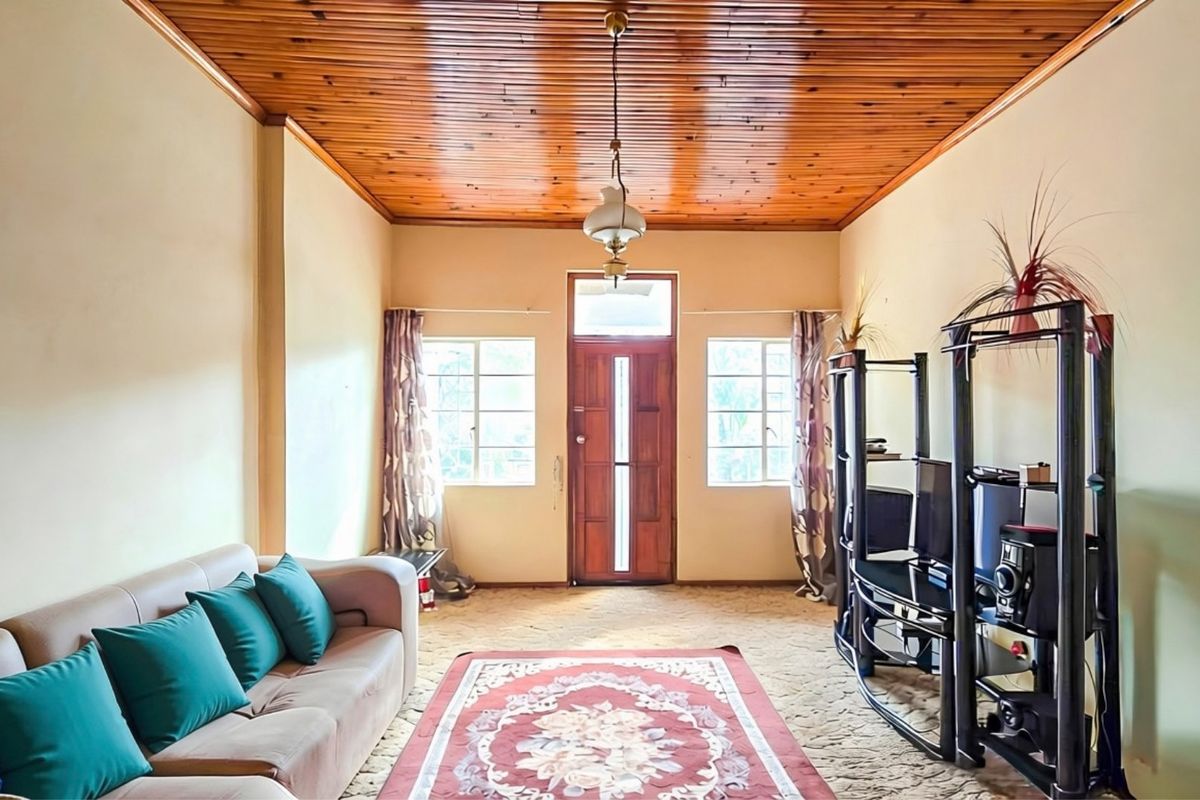 A living room featuring a warm timber tongue and groove ceiling, natural light through casement windows, and a classic timber entrance door.