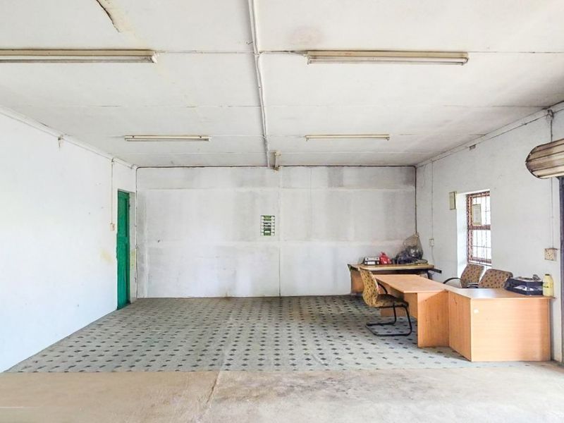 A functional commercial office space featuring tiled flooring, fluorescent lighting, and a roller shutter door, offering a versatile layout for business operations.