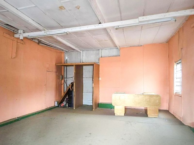 An empty utility or storage space featuring corrugated metal wall cladding, exposed ceiling beams, and basic fluorescent lighting, requiring cosmetic refurbishment.