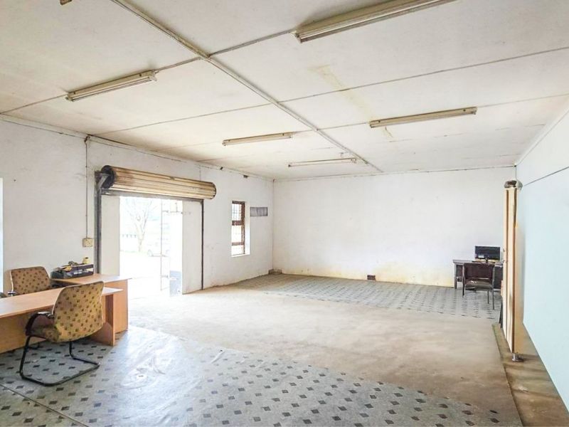 Spacious commercial office area featuring tiled flooring, fluorescent lighting, and a roller shutter door, offering a functional workspace with potential for modernization.