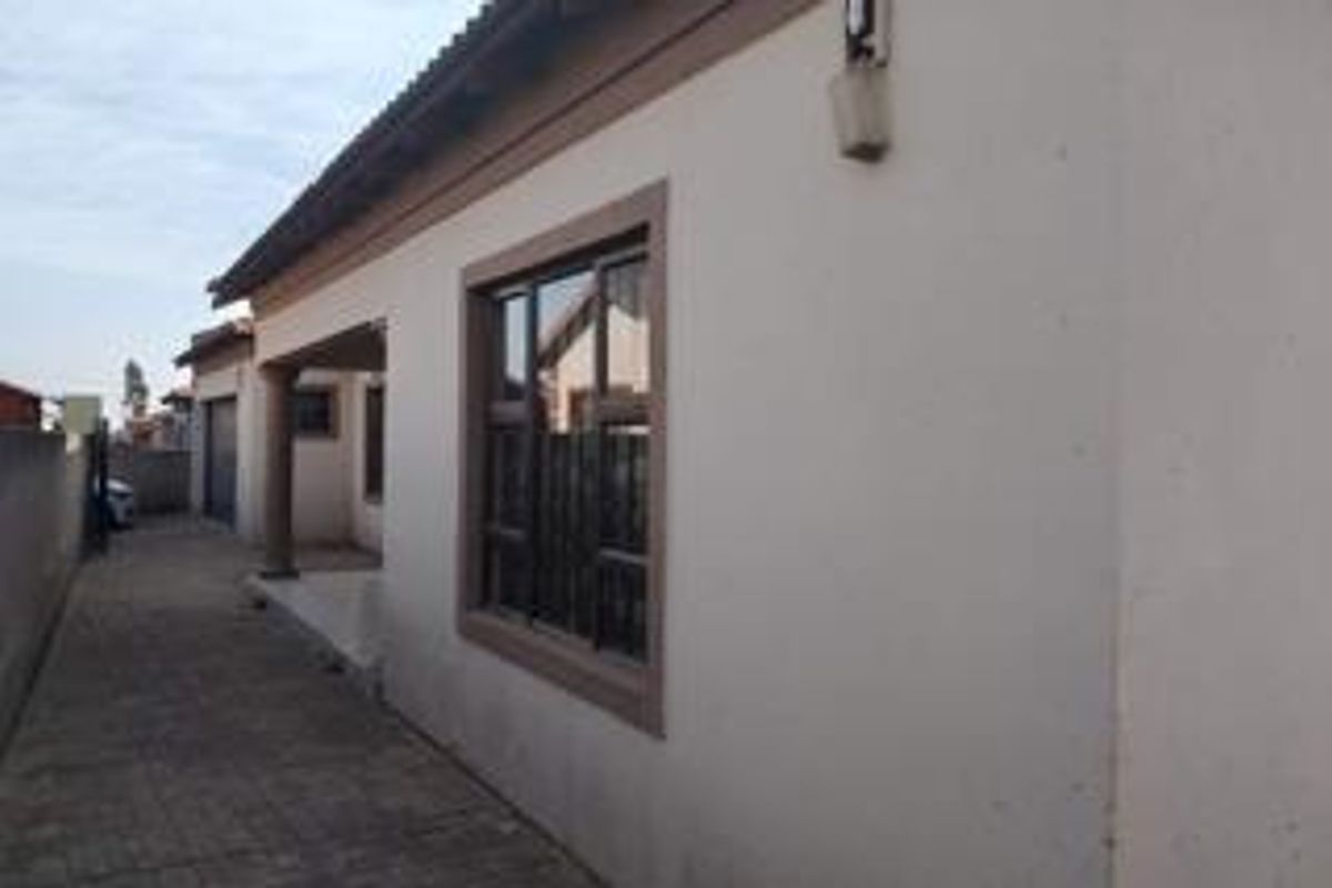 Side view of the property showing a paved driveway, exterior wall finishes, and aluminium window frames.