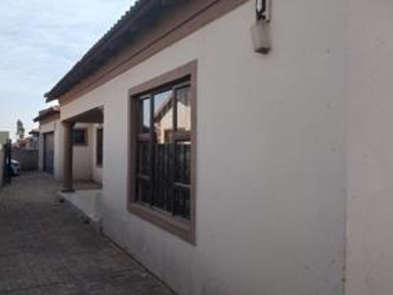Side view of the property showing a paved driveway, exterior wall finishes, and aluminium window frames.