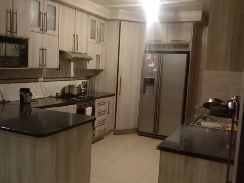 A functional kitchen featuring light wood-grain cabinetry, dark granite countertops, built-in appliances, and tiled flooring, offering ample storage and workspace.