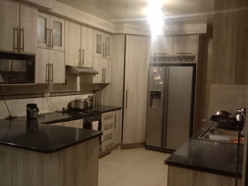 A functional kitchen featuring light wood-grain cabinetry, dark granite countertops, a gas hob, extractor fan, and integrated appliances with tiled flooring.
