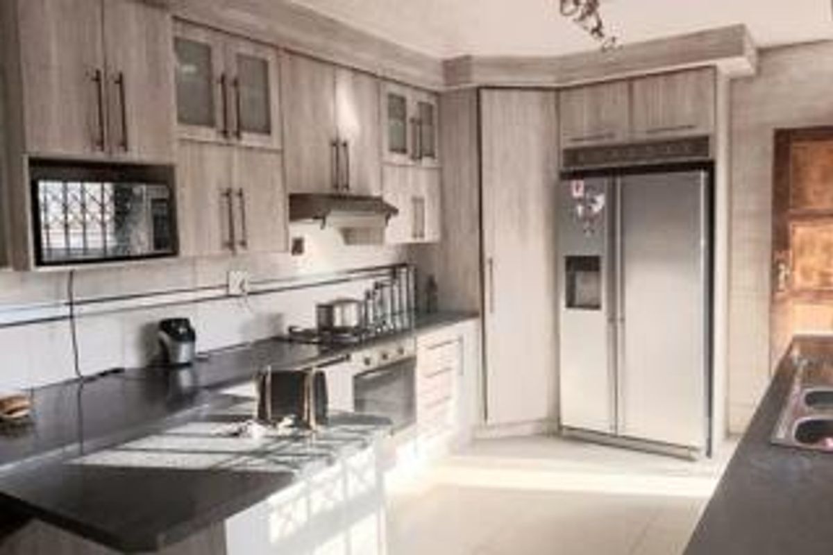 A functional kitchen featuring light wood-grain cabinetry, dark stone countertops, integrated appliances, and a double sink, offering a clean and practical workspace.