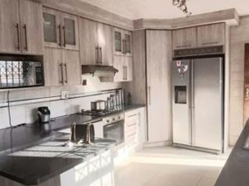 A functional kitchen featuring light wood-grain cabinetry, dark stone countertops, integrated appliances, and a double sink, offering a clean and practical workspace.