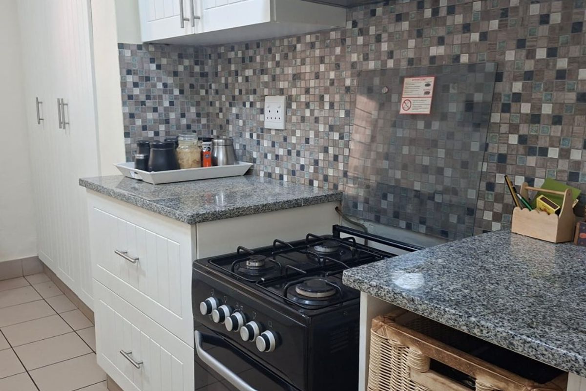 A functional kitchen featuring white cabinetry, granite countertops, a mosaic tile backsplash, and a freestanding gas stove with an overhead extractor fan.