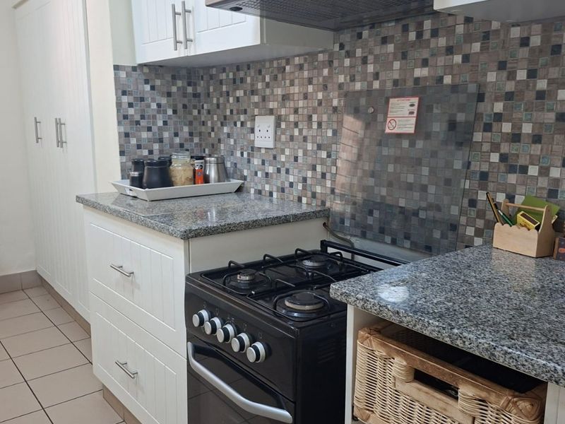 A functional kitchen featuring white cabinetry, granite countertops, a mosaic tile backsplash, and a freestanding gas stove with an overhead extractor fan.