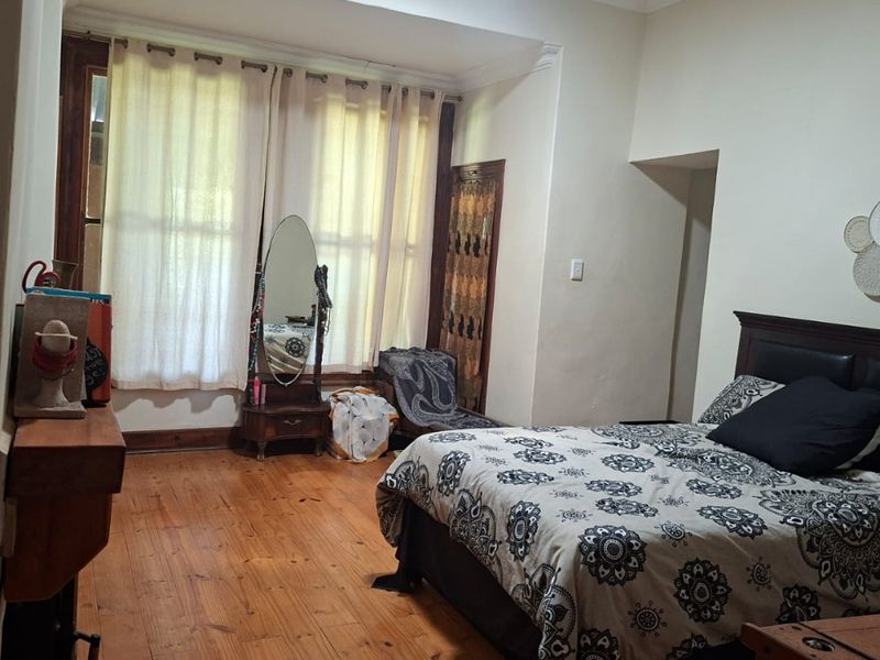 Spacious bedroom featuring original hardwood flooring, a fireplace, and large sash windows that provide ample natural light.