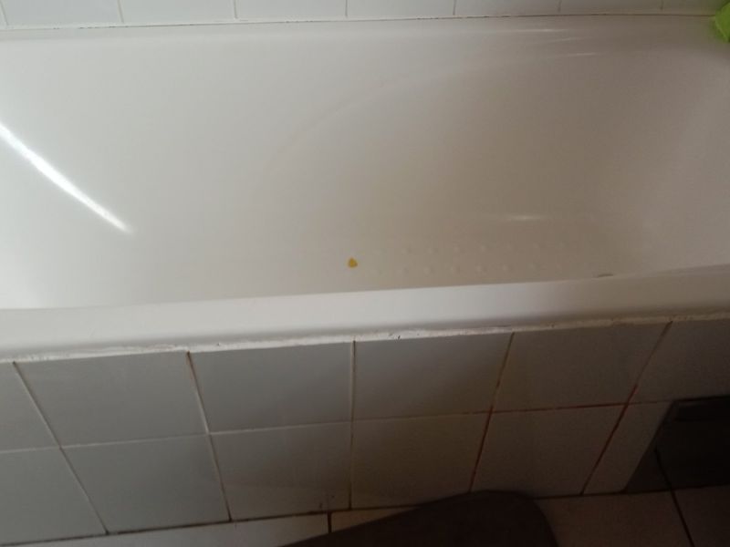 A standard bathroom featuring a built-in bathtub with tiled apron and chrome fixtures, showing signs of wear and discolored grout.