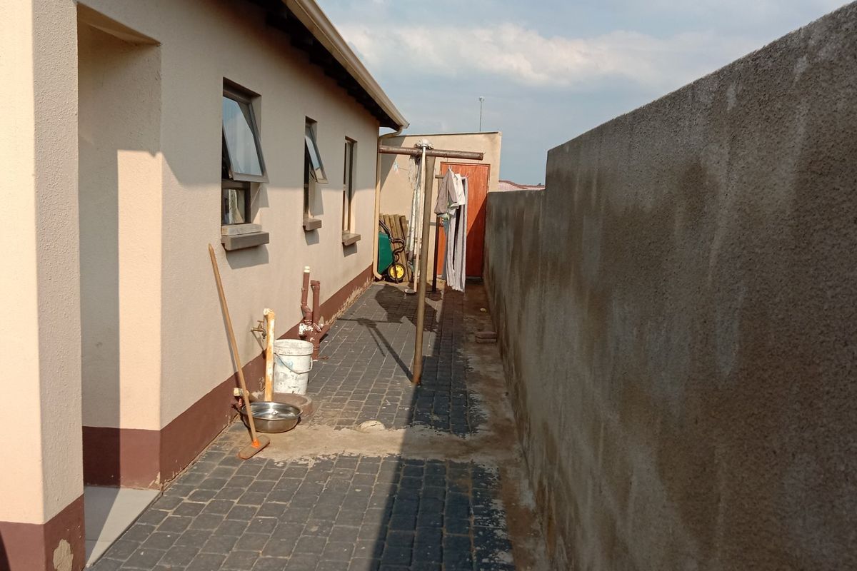 A side exterior walkway featuring paved flooring, external plumbing fixtures, and a high boundary wall along the side of the house.
