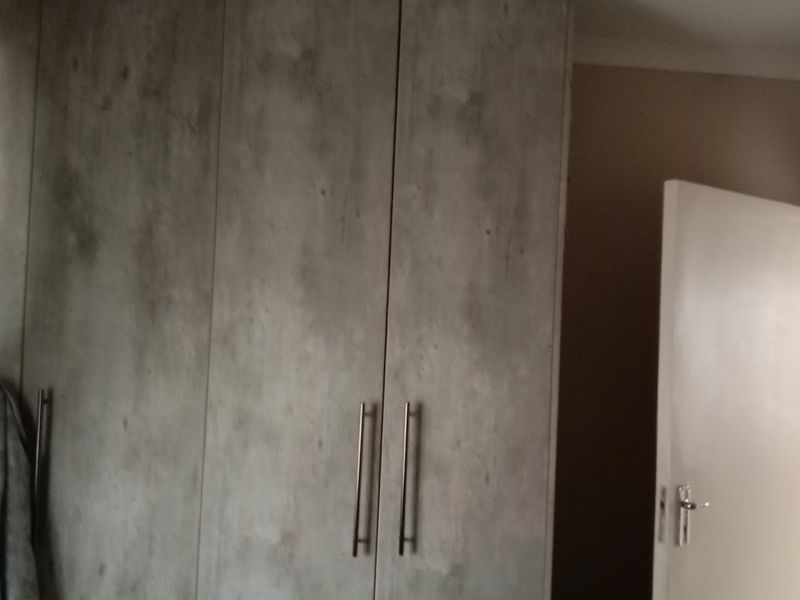 A bedroom featuring modern grey-toned built-in cupboards with sleek metal handles and neutral wall finishes.